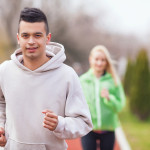 Handsome young man jogging on running track in a park. Unrecognizable woman jogging in the background.