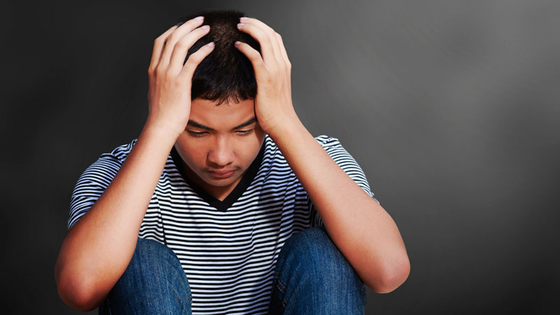 a young person sitting with head in hands, troubled